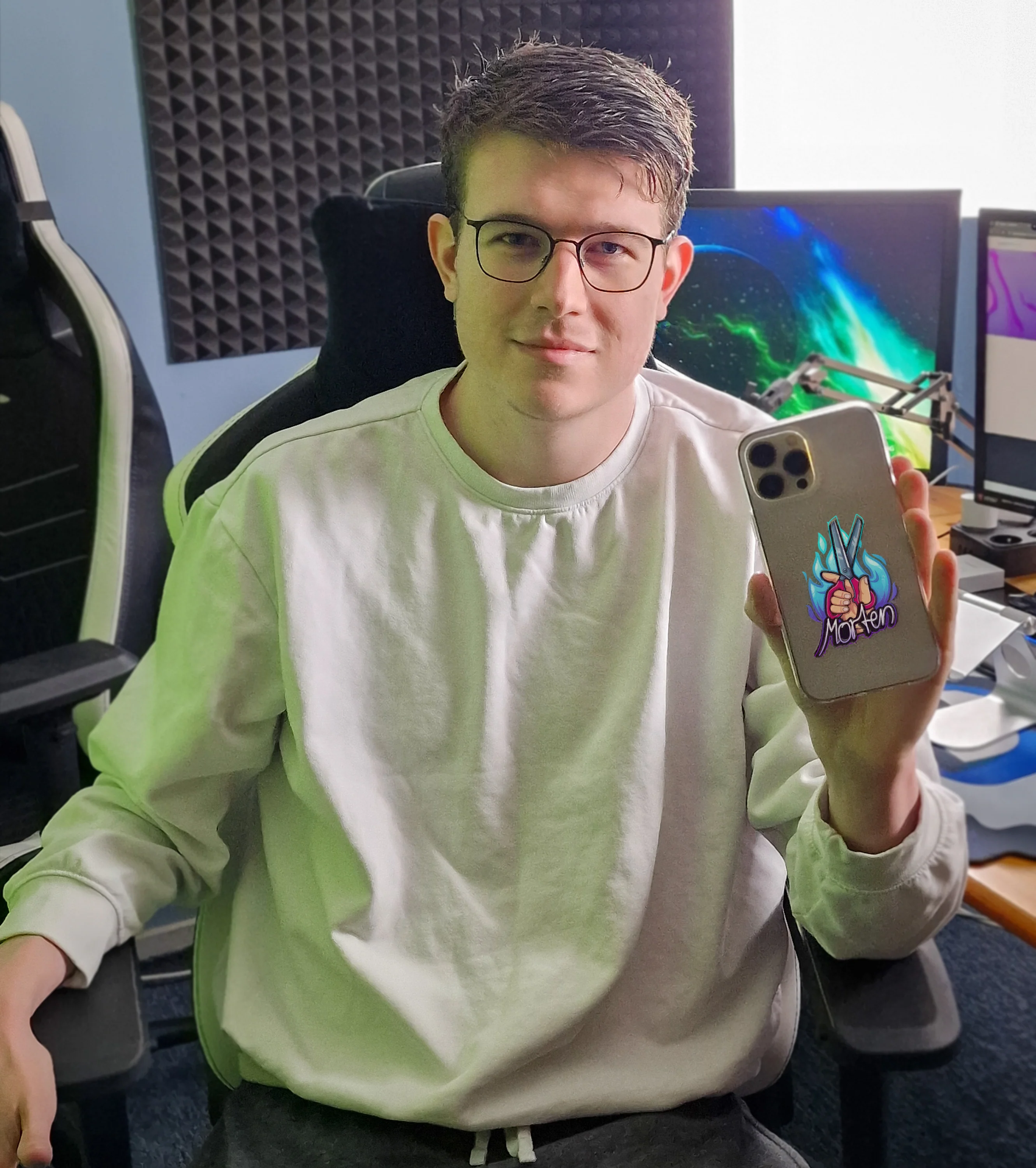Morten zeigt seine eigene Handyhülle mit flammendem Scheren-Design vor seinem Gaming-Setup – perfektes Creator-Produktbild für Fans.