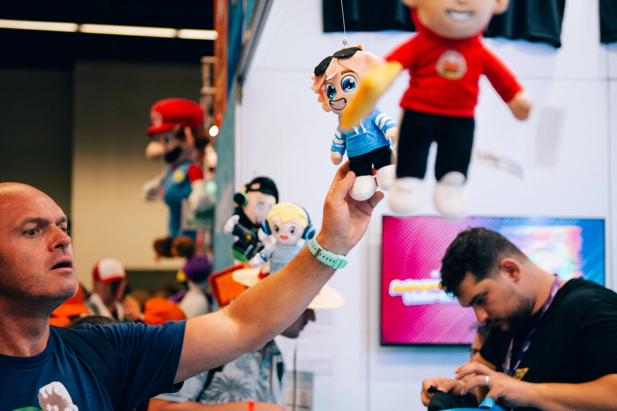 Besucher greift nach einem hängenden Creator Plushie am LunyMerch Stand auf der gamescom 2026